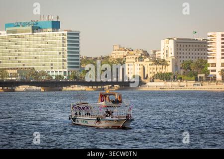 Ein traditionelles ägyptisches Felukenboot mit farbenfrohen, dekorativen Baldachinen bringt Touristen auf dem Nil in Kairo mit modernen Hochhäusern und seinen Gästen Stockfoto