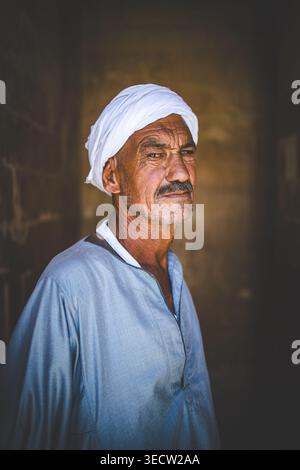 SAKKARA, KAIRO, ÄGYPTEN – 24. MAI 2025: Ein älterer ägyptischer Mann mit weißem Turban und hellblauer Galabiya steht im antiken Sakkara-Komplex Stockfoto
