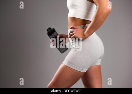 Frau in weißer Trainingskleidung, die im Fitnessstudio eine Wasserflasche hält Stockfoto