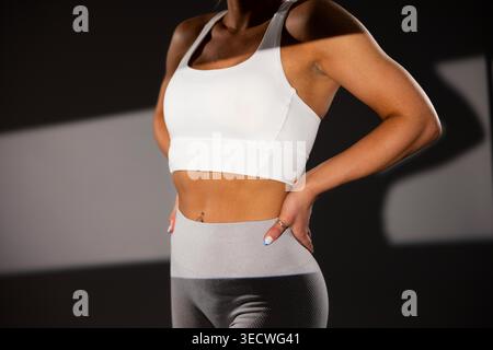 Eine Frau mit weißem Sport-BH und grauer Leggings steht selbstbewusst im Fitnessstudio Stockfoto