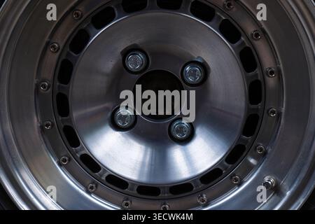 Technische Nahaufnahme einer modernen polierten silbernen Leichtmetallfelge mit sichtbaren Schrauben und einer markanten gebürsteten Metallstruktur. Stockfoto