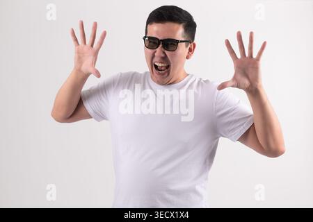 Junger Mann in einem weißen T-Shirt, der mit Händen ein komisches Gesicht macht Stockfoto