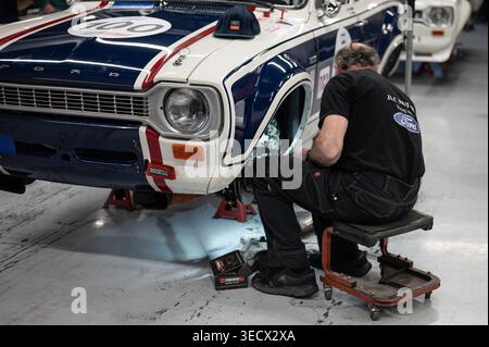 Mechaniker, der in einer Werkstatt an der Vorderradaufhängung und den Bremsen eines klassischen Ford Escort Mk1 RS1600 Rennwagens arbeitet. Stockfoto