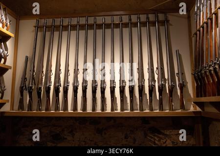 Wandregal mit historischen Langkanonen und Feuersteinmusketen in der Rüstungsausstellung im Tower of London, London, England, Vereinigtes Königreich. Stockfoto