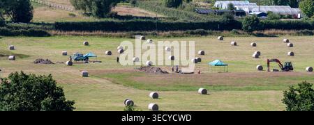 Ländliches Feld mit runden Heuballen, Zelten und Maschinen auf dem Land in der Nähe von Bodiam, East Sussex, England, Vereinigtes Königreich. Stockfoto