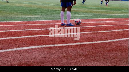 Nahaufnahme eines jungen Fußballspielers, der mit Fußball auf der roten Laufbahn neben dem grünen Sportfeld während des Outdoor-Trainings steht. Stockfoto