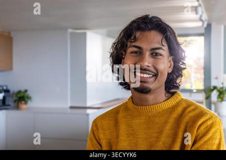 Asiatischer erwachsener Mann lächelnd, stehend in der modernen Küche mit Senfpullover in der Nähe einer Kaffeemaschine Stockfoto