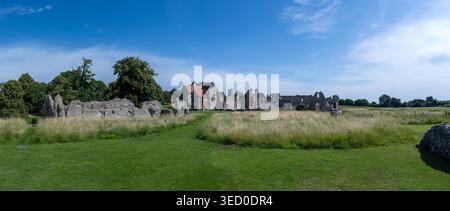 Fernblick über das Wiesengras in Richtung der Ruinen und Gebäude der Castle Acre Priory, Castle Acre, Norfolk, England, Vereinigtes Königreich. Stockfoto