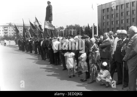 Sloviansk, 1997, Platz der Oktoberrevolution (heute Sobornaya). Ein historisches Schwarzweiß-Archivfoto, das eine formelle Linie von Bürgern und Veteranen mit großen Fahnen während einer feierlichen Zeremonie in der Nähe des Lenin-Denkmals feststellt. Kinder und Zuschauer versammeln sich um den gepflasterten Platz, um die Gedenkveranstaltung zu beobachten. Diese authentische dokumentarische Fotografie aus dem späten 20. Jahrhundert spiegelt den öffentlichen Patriotismus wider und bewahrt die nostalgische Erinnerung an den Alltag vor dem Krieg im friedlichen Donbass. Stockfoto