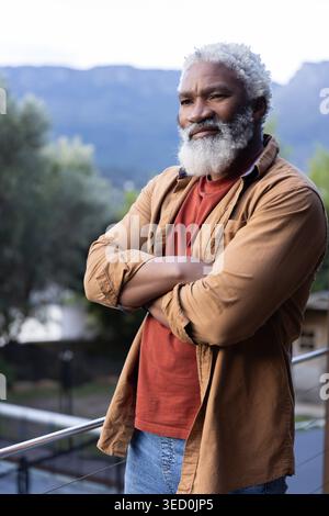 Ranghöchster afroamerikanischer Mann, der sich auf einen Balkon stützt, in braunem Hemd und Jeans, und den Talkamm sieht Stockfoto