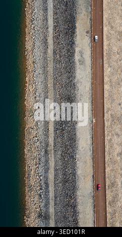 Autos fahren entlang einer Straße entlang einer felsigen Küste, während Wellen die Küste treffen. Das Wasser ist blau und klar und bietet einen friedlichen Blick auf die Natur. Stockfoto
