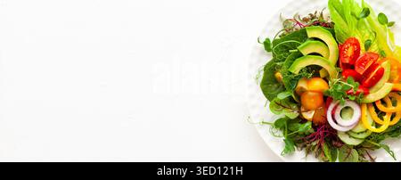 Köstlicher, gesunder Salat mit frischer Avocado, Tomaten, Gurken, Paprika, Salat, Mikrogreens auf weißer Platte. Sauberes Essen, Mittagsschüssel. Draufsicht. Stockfoto
