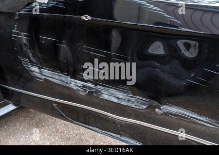 Nahaufnahme des beschädigten schwarzen Fahrzeugs. Autoreparaturfoto mit Kratzern und Blendeffekten. Detaillierte Abbildung der schwarzen Autotür mit Einbuchtung Stockfoto