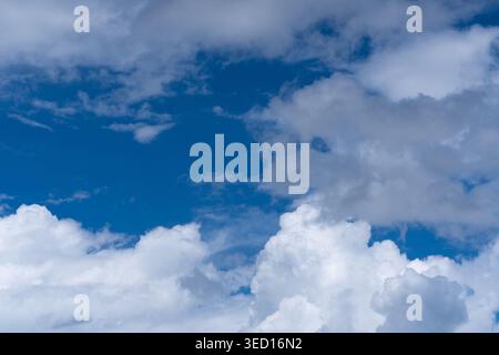 Ein malerischer Blick auf große, hoch aufragende weiße Cumulus-Wolken hinter einem üppigen grünen Hügel und einem traditionellen rostigen Zinkdach. Dieses Bild stellt eine typische Brig dar Stockfoto