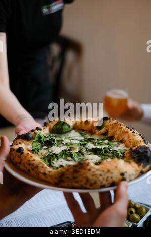 Vegetarische neapolitanische Pizza mit frischem Spinat, geschmolzenem Mozzarella und cremiger Gorgonzola, serviert auf einem weißen Teller und zum Tisch gebracht Stockfoto