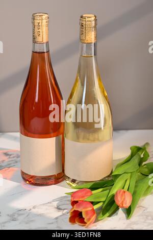Zwei Flaschen Wein stehen neben frischen Tulpen auf Marmor. Stockfoto