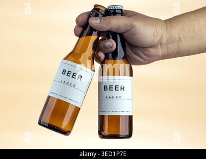 Studio-Nahaufnahme einer Hand, die zwei Braunglasflaschen mit sauberen, minimalistischen weißen Etiketten packt. Etiketten wie Beer Lager, handgefertigt, 5,0% ab Stockfoto