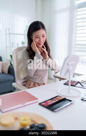 Junge asiatische weibliche Beauty-Vloggerin, die roten Lippenstift aufträgt, während sie ein Make-up-Tutorial im hellen modernen Zuhause aufnimmt Stockfoto