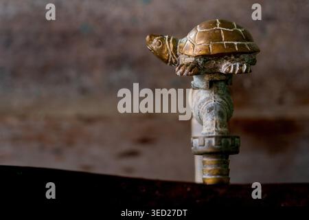 Ein Nahaufnahme eines kunstvollen, Vintage-Wasserhahns aus Messing mit einem einzigartigen Griff in Form einer Schildkröte. Das Metall zeigt eine schöne alte Patina und W Stockfoto