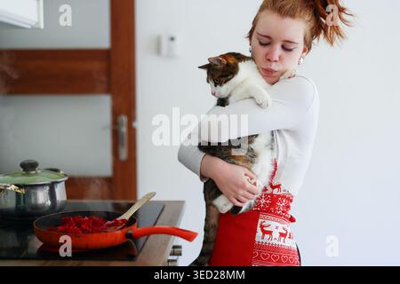 Frau, die Katze in der Nähe des Herds mit kochender Mahlzeit, Tierliebe und Lebensstil-Moment zu Hause. Stockfoto