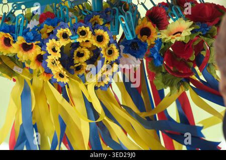 Farbenfrohe Blumenkronen hängen von der Ausstellung eines Händlers auf einem geschäftigen Markt im Freien. Stockfoto
