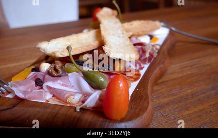 Blick aus nächster Nähe auf die Vorspeisenplatte mit erstklassigem italienischem Aufschnitt einschließlich Schinken und Salami. Das hölzerne Servierbrett mit Käse c Stockfoto
