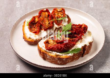 Toast mit Frischkäse und getrockneten Tomaten. Offenes Sandwich mit Rucola, Brot, Tomaten, Oliven und Öl. Stockfoto
