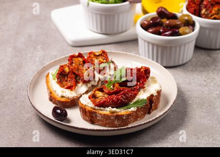 Toast mit Frischkäse und getrockneten Tomaten. Offenes Sandwich mit Rucola, Brot, Tomaten, Oliven und Öl. Stockfoto