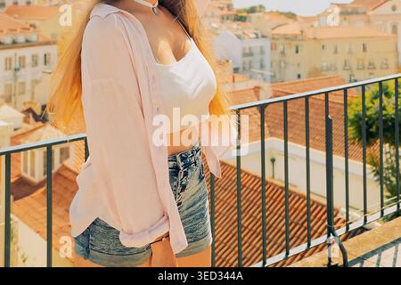 Frau genießt sonnigen Tag mit Blick auf die Stadt und das Meer, während sie auf dem Balkon in Lissabon steht. Blick auf die Stadt und das Meer. Sie hebt ihre Arme in die Luft, Stockfoto
