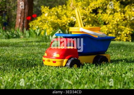Ein leuchtend roter und blauer Spielzeugwagen sitzt auf grünem Gras Stockfoto