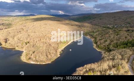 Das Prada-Reservoir reflektiert den Himmel, umgeben von Hügeln, die mit Bäumen bedeckt sind und Vegetation unter wechselndem Himmel in der Nähe von A veiga, ourense Stockfoto