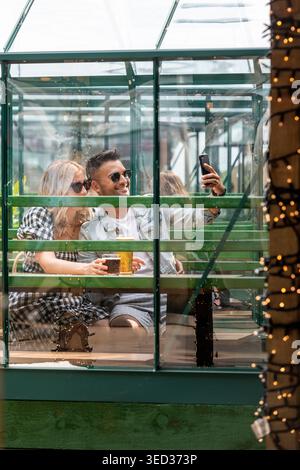 Paare, die Selfie machen, während sie draußen trinken, im Stadtzentrum von Manchester, England, Großbritannien Stockfoto