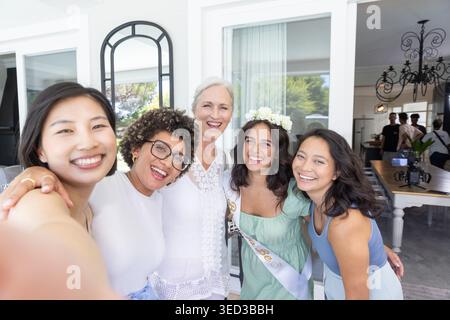 Verschiedene weibliche Freunde machen GruppenSelfie im Essbereich, Braut trägt Schärpe und Krone Stockfoto