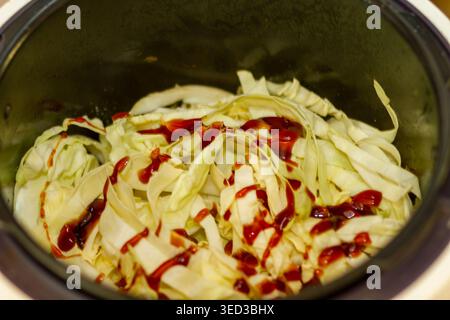 Frisch gehackter Weißkohl mit roter Sauce in einem Kochtopf. Zubereitung von traditionellem Gemüseeintopf für den Kohl-Crush-Trend. Stockfoto