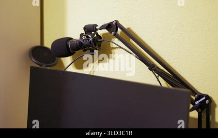 Podcast-Aufnahmeeinrichtung mit Kondensatormikrofon am Ausleger, Stoßhalterung und Popfilter über dem Computermonitor im Innenbereich. Stockfoto