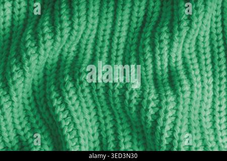 Nahaufnahme, Makro aus zerknittertem, grünem Strickgewebe mit sichtbaren Falten, Falten und weichen Wellen. Weiche Wollstruktur mit detaillierten Nähten und Falten, na Stockfoto