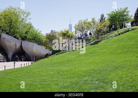 Besucher erkunden den üppigen Hügel des Little Island Parks mit dem One World Trade Center in der Ferne, New York City, 1. Mai 2026. Stockfoto