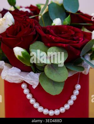 Lebendige Rosen und Grünpflanzen in einer roten Schachtel mit Perlen, die im Innenraum ausgestellt ist Stockfoto