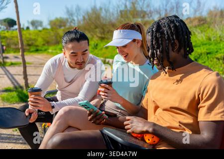 Verschiedene Freunde, die eine Picknickpause genießen, Kaffee trinken, sich das Smartphone ansehen Stockfoto
