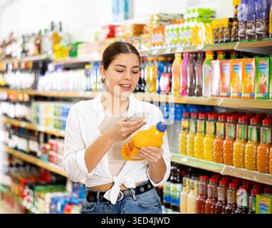 Junge Frau, die im Internet im Supermarkt nach Informationen über Säfte sucht Stockfoto