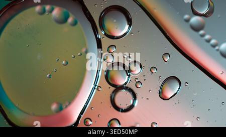 Makroansicht von Öl im Wasser mit weichem Bokeh und warmen rosa zu goldenen Farbübergängen Stockfoto