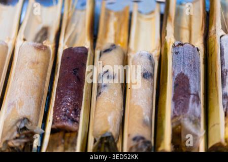 Nahaufnahme von klebrigen Reisrollen, die in Bambusröhren gegrillt werden und traditionelle Street Food Textur rauchiger Geschmack natürliche Kochmethode zeigen Stockfoto