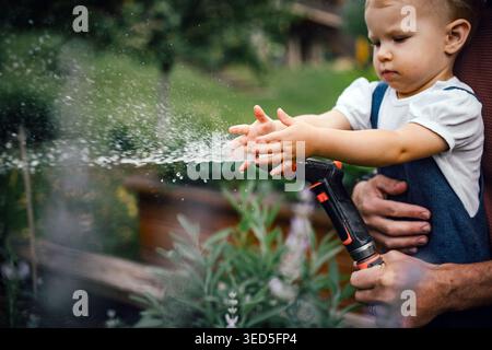 Nahaufnahme von Kindern, die mit Schlauch spielen und Pflanzen bewässern. Stockfoto