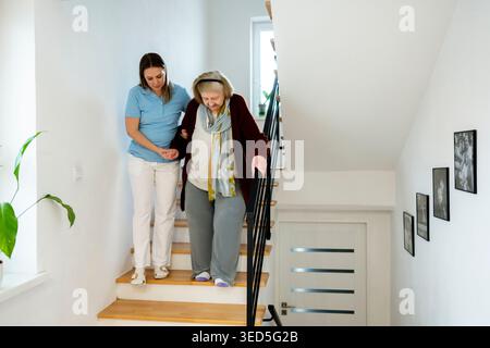 Schwester hilft der alten Frau, die Treppe hinunter zu gehen. Stockfoto