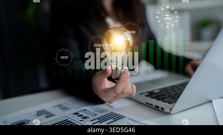 Eine Geschäftsfrau hält eine glühende Glühlampe, die Innovation und nachhaltiges Wachstum symbolisiert, und zeigt gleichzeitig Finanzgrafiken und zukünftige Ziele in einem Stockfoto