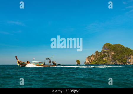 Traditionelles thailändisches Langboot, das über die Andamanensee in der Nähe von Kalksteinklippen und tropischen Inseln in Koh Phi Phi, Provinz Krabi, Thailand fährt. Stockfoto