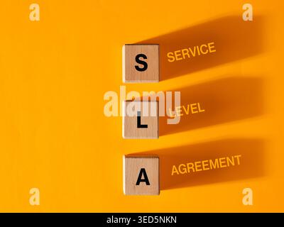 Drei Holzwürfel mit Abkürzung SLA, Service Level Agreement auf gelbem Hintergrund. Stockfoto