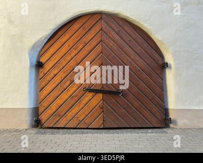 Historisches bogenförmiges Holztor in alter Putzmauer - geeignet für Themen der historischen Architektur, des Eingangsdesigns, des Kulturerbes und der traditionellen Handwerkskunst Stockfoto
