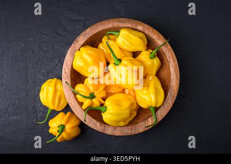 Holzschale gefüllt mit gelben Habanero-Paprika auf dunklem Hintergrund. Frische Chilischoten natürliche Zusammensetzung minimales Styling Stockfoto
