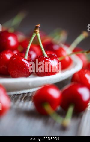 Frische süße Kirschen in kleiner Schüssel auf rustikalem Holztisch, geringe Tiefe. Reife rote Kirschen mit Stielen, Sommerfrucht-Konzept Stockfoto